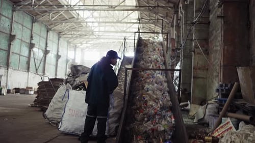 A Young AfricanAmerican Woman Checks a Conveyor Belt at a Recycling Plant