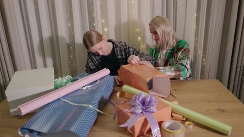 Two People Wrapping Gifts Together at Table