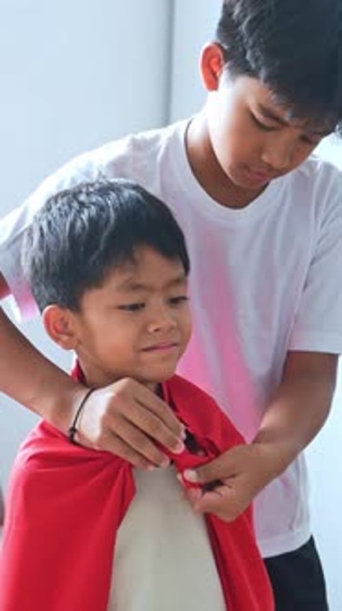 Close up Older brother helps younger sibling dress as superhero at home