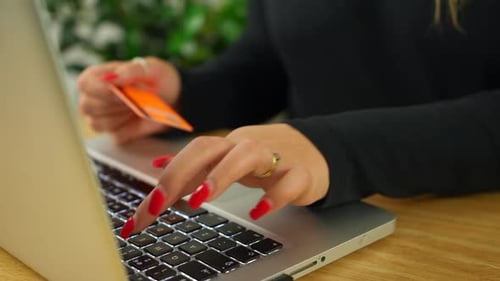 An unrecognizable blonde woman paying online using a credit card and a laptop