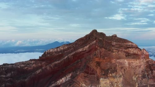 Red Rock Mountain Cliff Peak Ridge in der Abenddämmerung, Drohnen-Luftaufnahme. Wolkiges Tal im Hintergrund. Rota