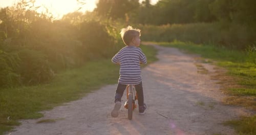 A Child Boy Rides Balance Bike in a City Park
