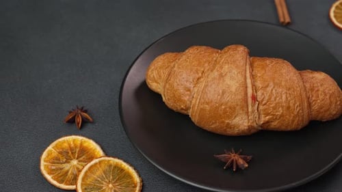 Close up of a delicious, freshly baked Croissant Lying on a black Plate against a black background