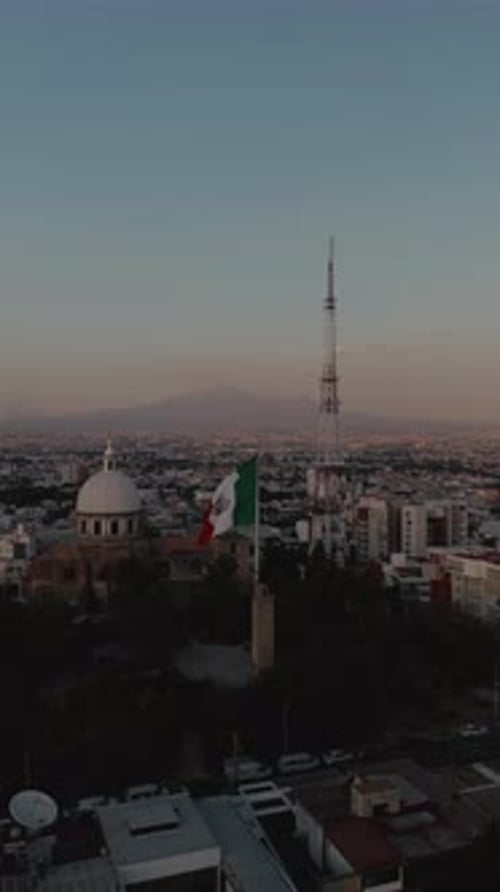 Vertical video of the Mexican flag waving in the wind during sunset, with Puebla City and the
