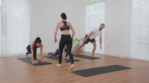 Group Yoga Class in a Bright Studio with Instructor Assisting Participants