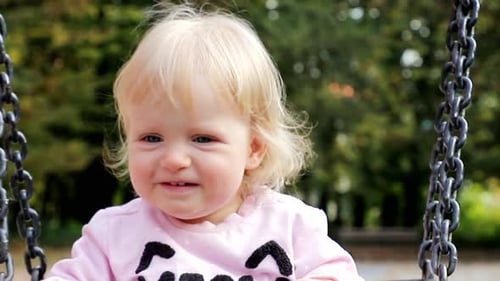 Little girl on a swing smiling and waving