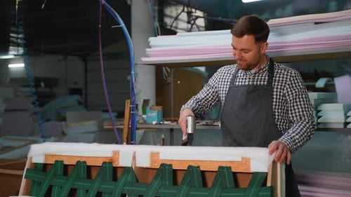 Upholsterer Securing Padding on Furniture Frame in Workshop