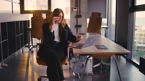 Businesswoman Working at Desk Talking on Smartphone