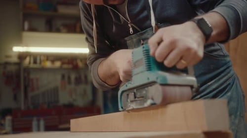 Man Sanding Wood With Belt Sander in Workshop