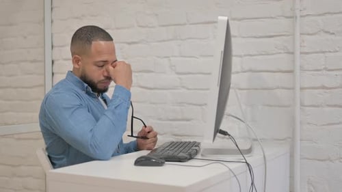 Man Rubs Eyes at Desk in Office