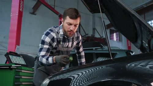 Using tool, changing parts. Man is repairing the car at a service station
