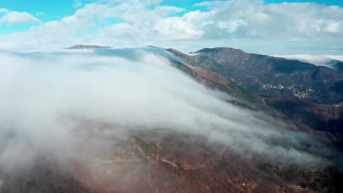 Clouds rolling over mountain peaks with clear blue sky, aerial view