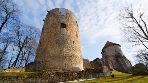 Low-angle view of medieval castle towers and stone ruins in bright spring light, with bare trees,
