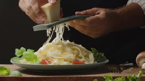 Chefkoch reibt Käse auf ein frisch zubereitetes Gericht mit gekochten Nudeln, traditionelles italienisches Essen