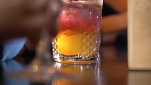 Bar counter with a cocktail, someone puts a glass in front