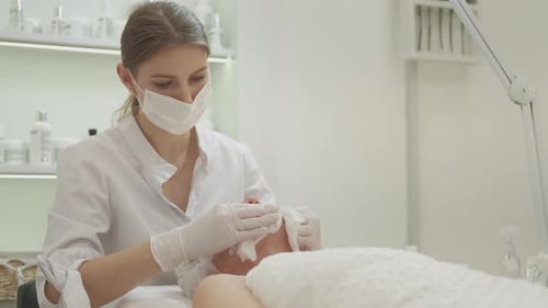 Cosmetologist Cleaning Mature Woman's Face at Clinic