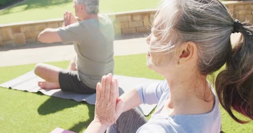 Happy diverse senior couple practicing yoga and meditating on mats in garden