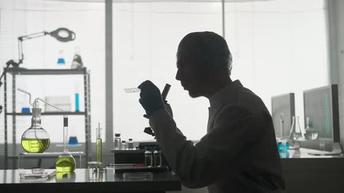 A Scientist in a Research Laboratory Examines a Sample on a Micropreparation Using a Microscope Side