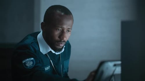 African American Security Officer Works in Monitoring Center During Night Shift