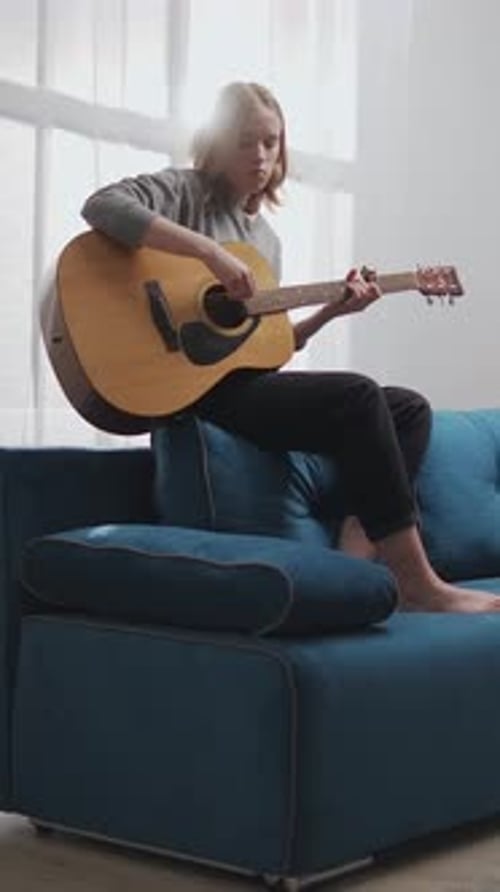 Young Woman Plays Acoustic Guitar on Blue Couch