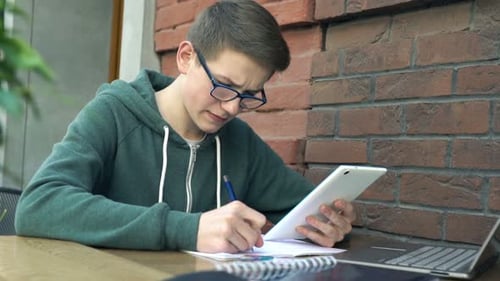 Teenager with Tablet and Notepad Doing Homework by Table in Cafe Adolescent