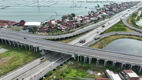 Aerial footage of highway traffic and intersection with watery landscape near residential area