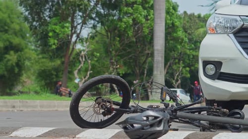 Crashed bicycle and helmet on road near white car illustrating traffic accident scene
