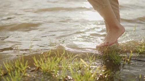 Close up of foot walking in the lake water and grass in sunset color and thinking about life.