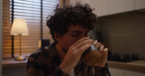 Close Up of a Happy Guy with Curly Hair Enjoying His Freshly Brewed Tea During His Breakfast in the