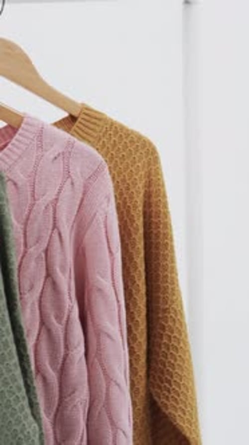 Vertical video of three multi coloured sweaters on hangers and copy space on white background