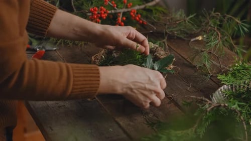 Young woman florist creating Christmas wreath in floral workshop.