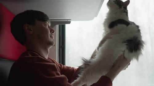Un propriétaire d'animal de compagnie monte dans un train avec son chat blanc et montre à un chaton curieux un wagon à compartiments