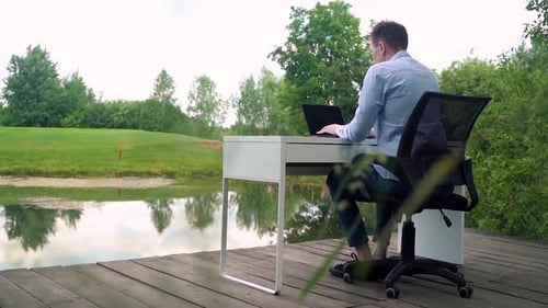 A man works at an office desk in nature near a river