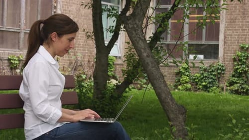 caucasian woman on a bench in a park with computer