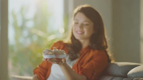 Pregnant Woman Holding Tiny Baby Shoes in Sunlight