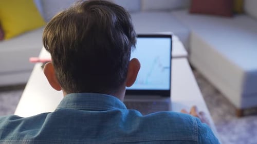 He has stock market and cryptocurrency investment from home with computer and writes notes.
