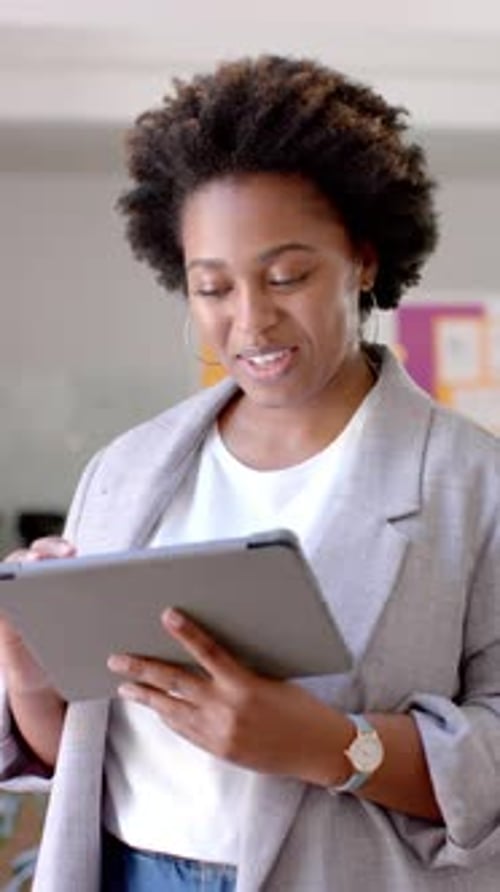 Vertical video of happy african american casual businesswoman using tablet in office, slow motion