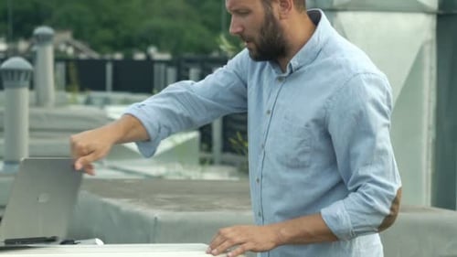 Young technician checks air conditioning system on city roof with laptop computer