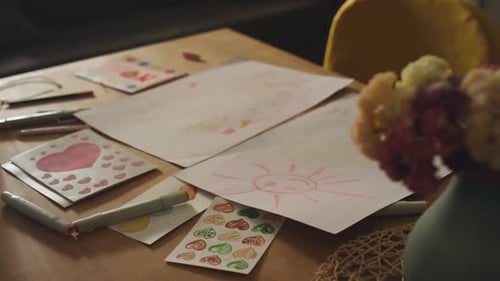 Childrens Drawings on Table with Color Markers and Flowers