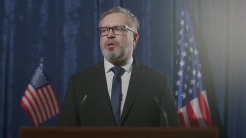 Man Giving a Speech at Podium with Flags