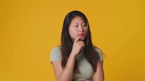 Young woman thinking and making decision isolated over yellow background in studio