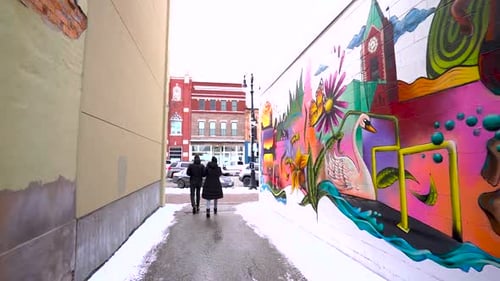 Walking down a snowy alley following people walking with graffiti on the wall.