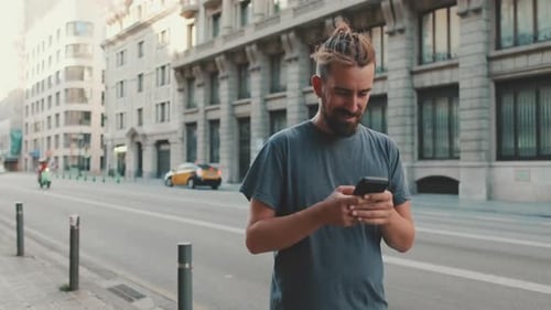Young smiling man with beard stands on street using cellphone