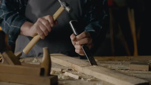 Sägewerk, Baumeister mittleren Alters arbeitet mit einem Meißel, indem er Späne aus dem Holz schlägt und mit Werkzeugen arbeitet