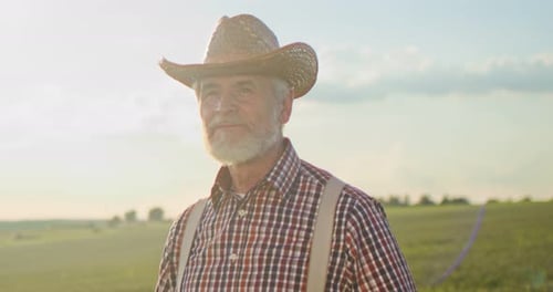 Portrait Shot of Attractive Senior Caucasian Man in Hat Standing in Green Field Smiling Cheerfully