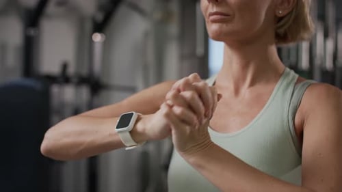 Adult Woman Warming up Wrists and Checking Smartwatch in Gym