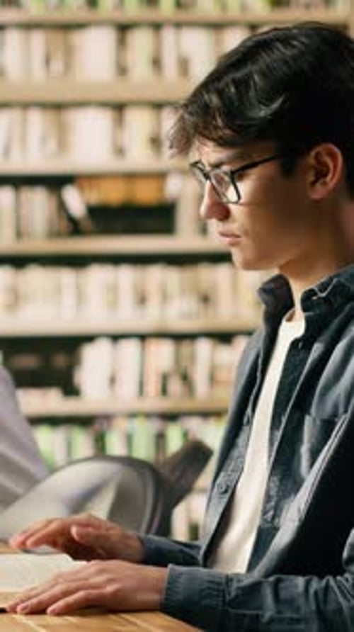 Vertical Video Young Asian Man with Glasses Reading Book at Library Study Table
