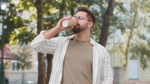 Happy Caucasian Young Man Tourist in Glasses Enjoying Morning Coffee Hot Drink on City Street