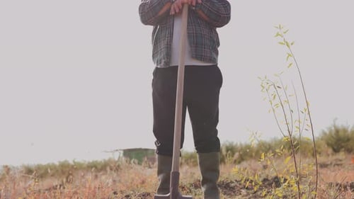Smiling Farmer with Shovel Standing on His Land