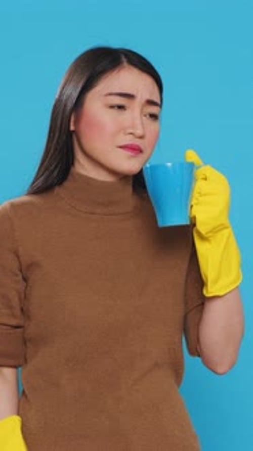 Vertical Video Pensive Thoughtful Maid Holding Cup of Coffee Standing Over Blue Background in Studio
